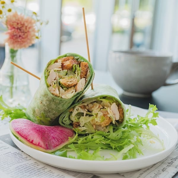 Two green wraps filled with chicken, lettuce, and croutons, served with a watermelon radish slice.