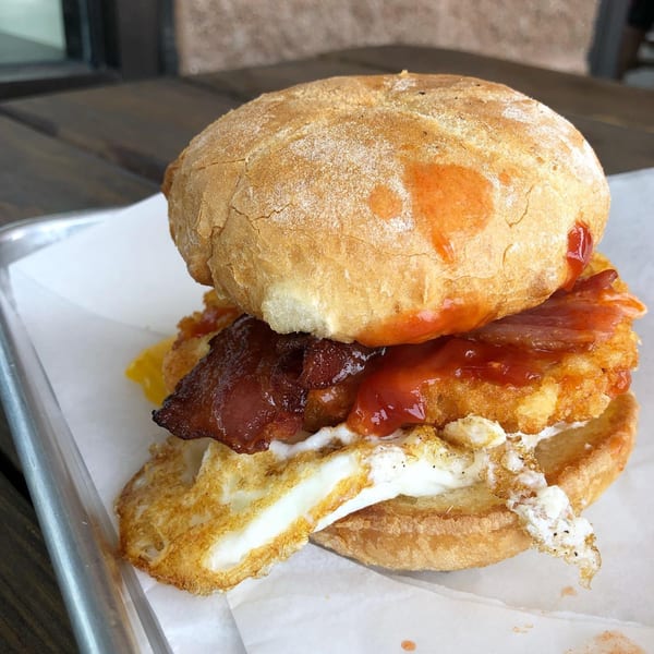A Bonnie & Clydes breakfast sandwich with egg, bacon, hash brown, and sauce on a bun.