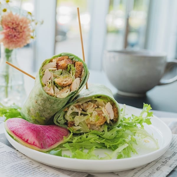 Two green wraps filled with chicken, croutons, and lettuce, served with a radish slice.