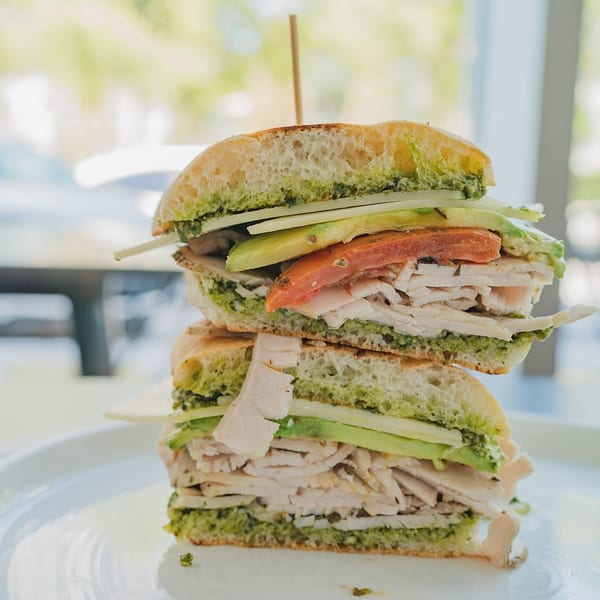 A stacked turkey and avocado sandwich with pesto on ciabatta bread, held by a toothpick.