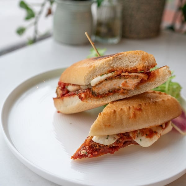 A chicken parmesan sandwich, cut in half, on a white plate with a side salad.