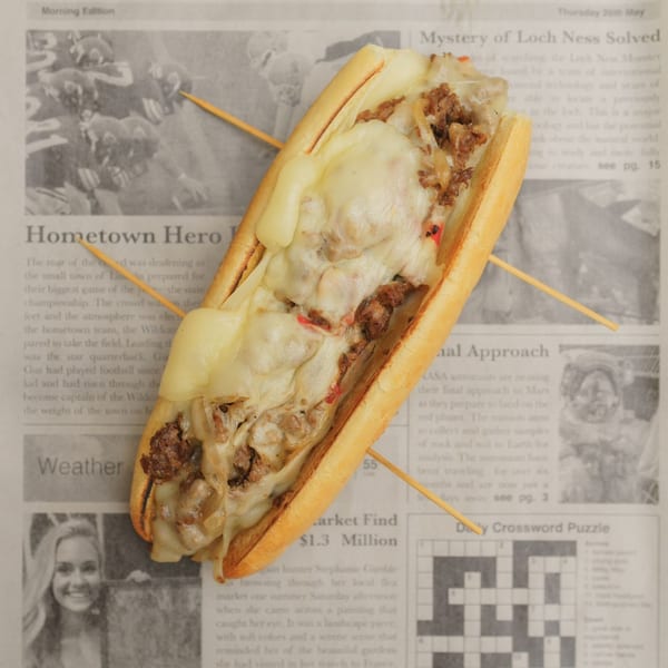 A cheesy steak sub with onions and peppers on a newspaper background at Bonnie & Clydes cafe.